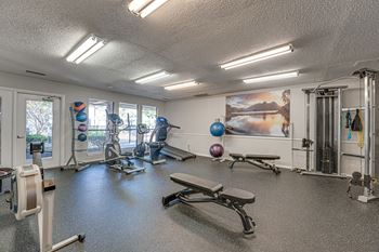 A gym with a variety of equipment including a rowing machine, a bench, and a squat rack.